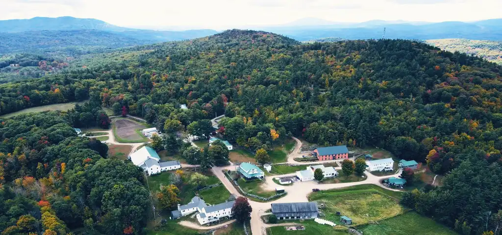 The His Mansion campus from the air in autumn, white buildings along a dirt road on a wooded hilltop