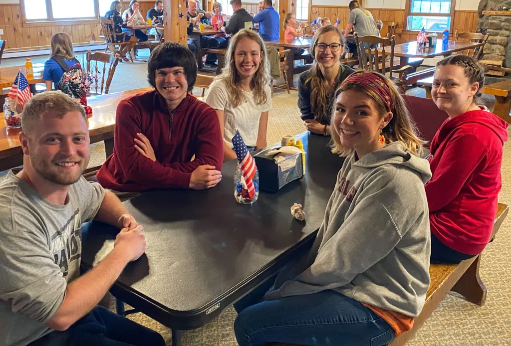 Six people sharing a Memorial Day meal at a table in Griggs Dining Hall, small American flags on the tables